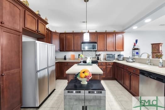 kitchen with a kitchen island, decorative light fixtures, stainless steel appliances, light countertops, and a sink