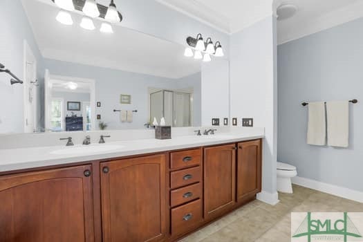 full bath featuring double vanity, a sink, toilet, and baseboards