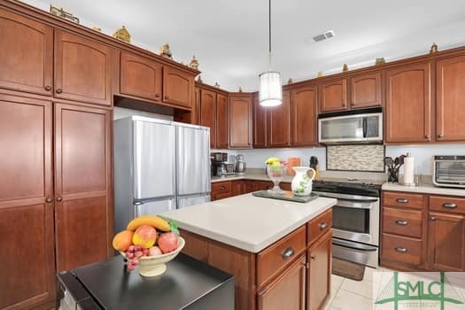 kitchen featuring visible vents, a kitchen island, brown cabinets, stainless steel appliances, and light countertops