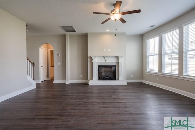 unfurnished living room with dark wood-type flooring, a glass covered fireplace, visible vents, and baseboards