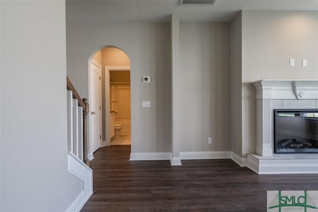 unfurnished living room featuring arched walkways, wood finished floors, baseboards, stairway, and a glass covered fireplace