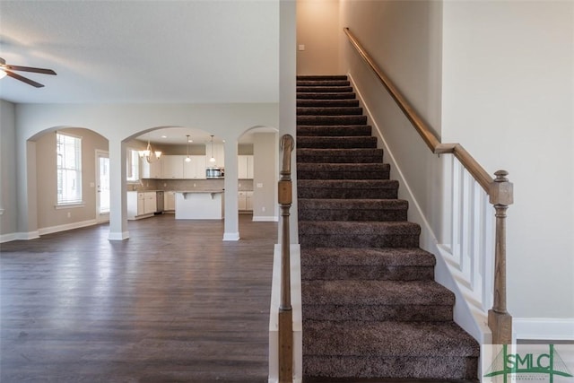 stairway featuring baseboards, arched walkways, wood finished floors, and ceiling fan with notable chandelier