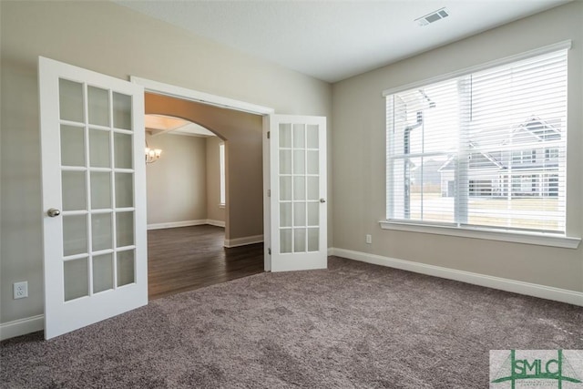 carpeted spare room with arched walkways, visible vents, baseboards, french doors, and an inviting chandelier