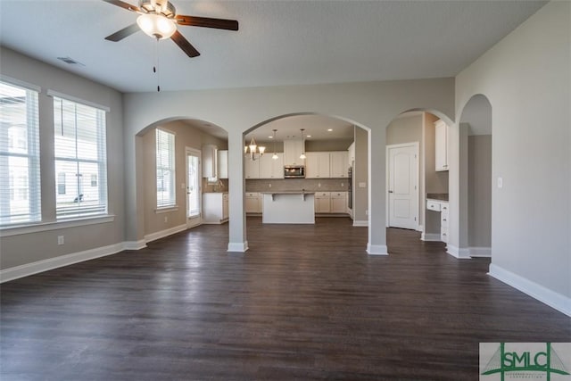 unfurnished living room featuring baseboards, visible vents, dark wood finished floors, and ceiling fan with notable chandelier