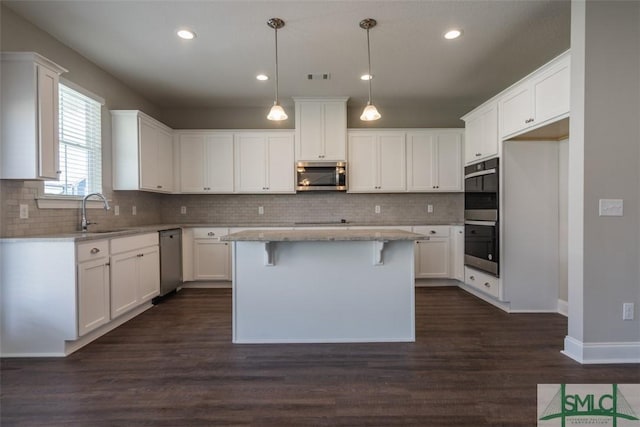 kitchen with appliances with stainless steel finishes, white cabinets, a sink, and a center island