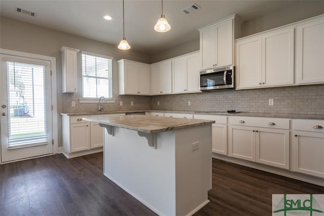 kitchen featuring dark wood-style floors, stainless steel microwave, visible vents, white cabinetry, and a kitchen island