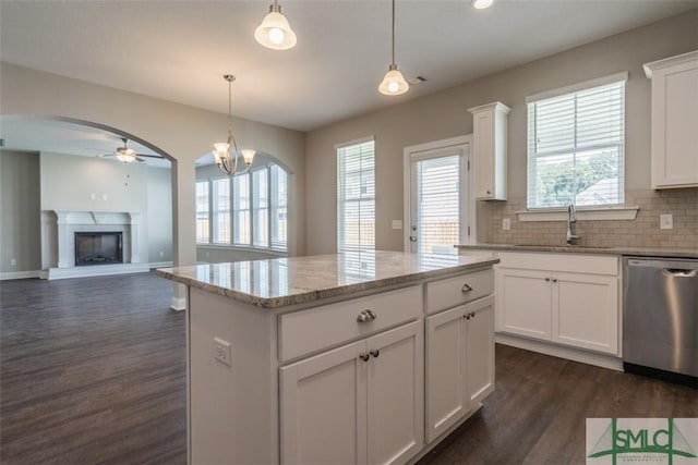 kitchen with dark wood finished floors, dishwasher, decorative backsplash, a fireplace with raised hearth, and a sink