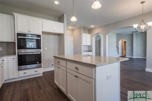 kitchen featuring stainless steel double oven, dark wood-style flooring, arched walkways, and backsplash