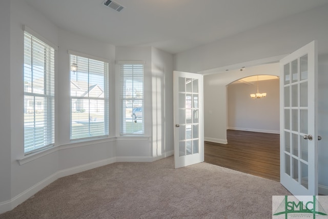 carpeted spare room with a healthy amount of sunlight, an inviting chandelier, and french doors