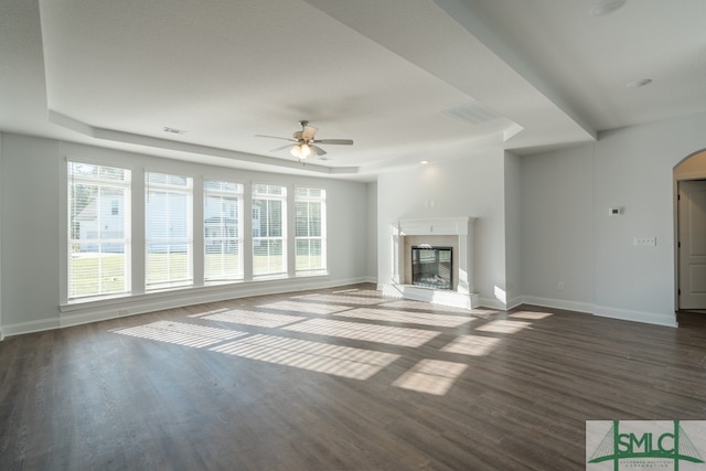 unfurnished living room with a tray ceiling, ceiling fan, and dark wood-type flooring