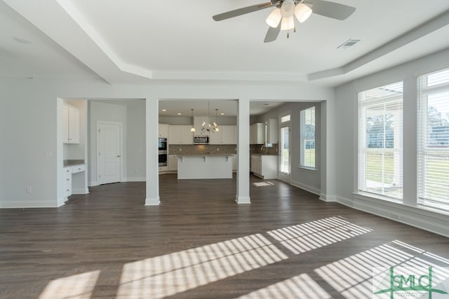 unfurnished living room featuring a raised ceiling, ceiling fan with notable chandelier, and dark hardwood / wood-style floors