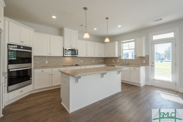 kitchen with appliances with stainless steel finishes, white cabinets, dark hardwood / wood-style floors, a kitchen island, and hanging light fixtures