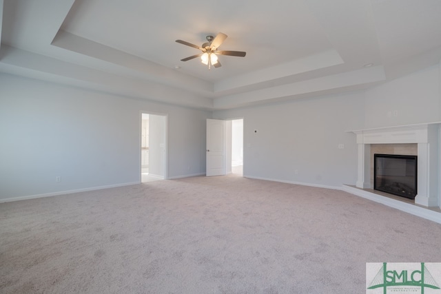 unfurnished living room featuring light carpet, a tray ceiling, and ceiling fan