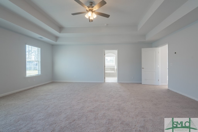 empty room with ceiling fan, light carpet, and a tray ceiling