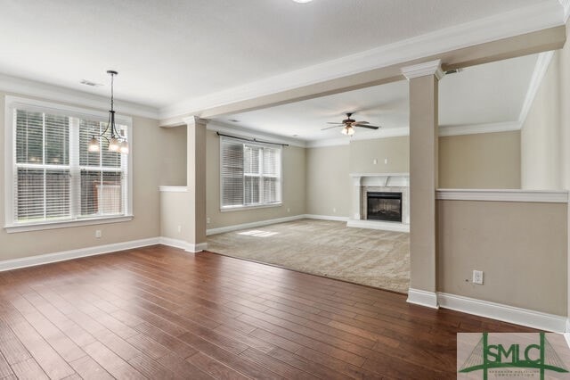 unfurnished living room featuring crown molding, dark wood-type flooring, ceiling fan with notable chandelier, and a wealth of natural light