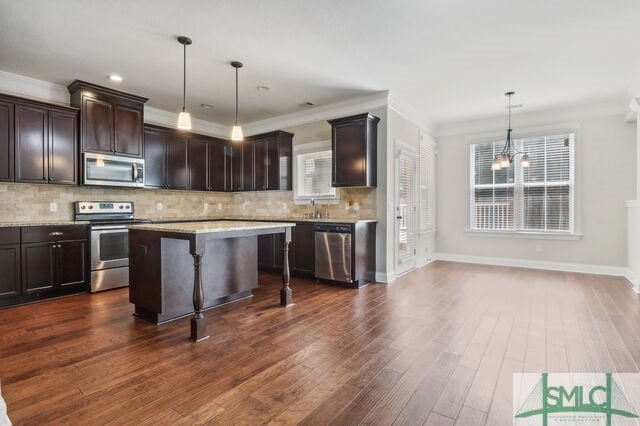 kitchen with a kitchen bar, appliances with stainless steel finishes, a notable chandelier, dark wood-type flooring, and a kitchen island