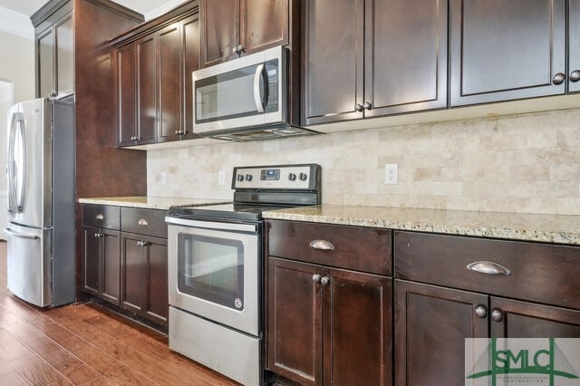 kitchen with appliances with stainless steel finishes, backsplash, light stone countertops, and dark wood-type flooring