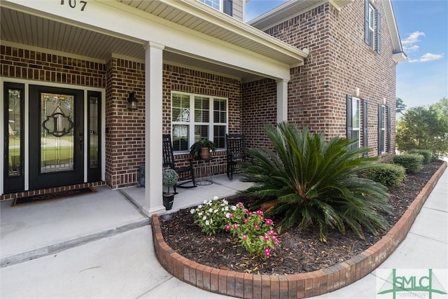 view of exterior entry featuring covered porch and brick siding