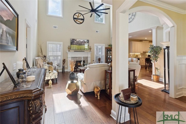 living room featuring ceiling fan, dark wood-style flooring, a fireplace, visible vents, and crown molding