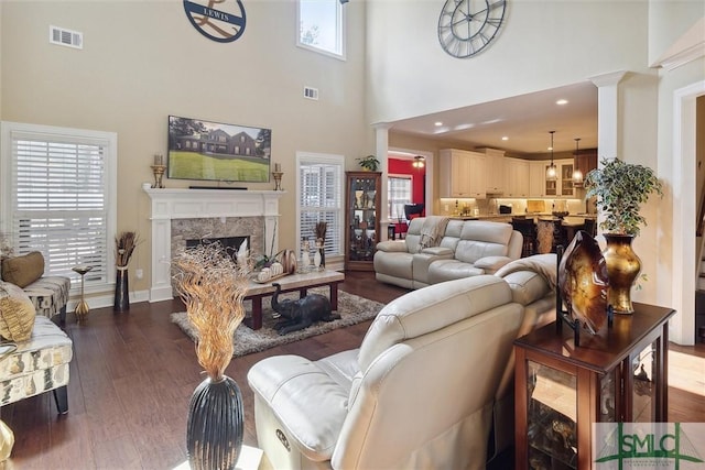 living room with decorative columns, a premium fireplace, visible vents, and dark wood finished floors