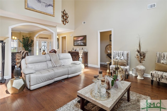 living area with crown molding, visible vents, arched walkways, and wood finished floors