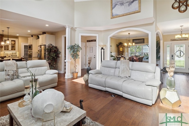 living room featuring a chandelier, ornamental molding, dark wood-style floors, and a towering ceiling