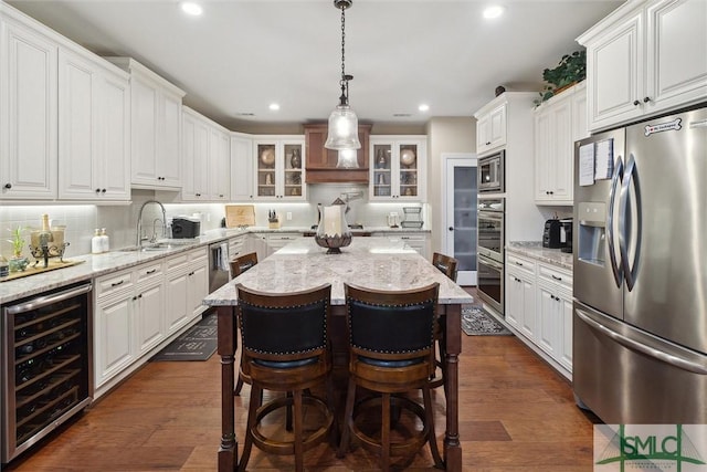 kitchen featuring beverage cooler, white cabinetry, appliances with stainless steel finishes, a center island, and glass insert cabinets