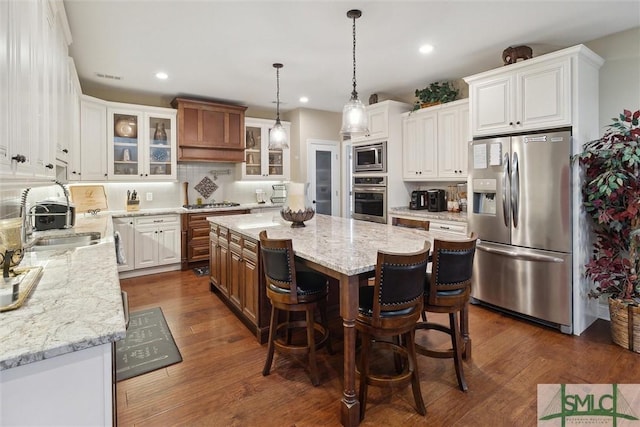 kitchen with light stone counters, stainless steel appliances, white cabinetry, a center island, and glass insert cabinets