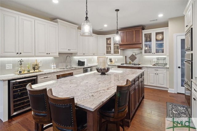 kitchen with wine cooler, glass insert cabinets, white cabinetry, a kitchen island, and a sink