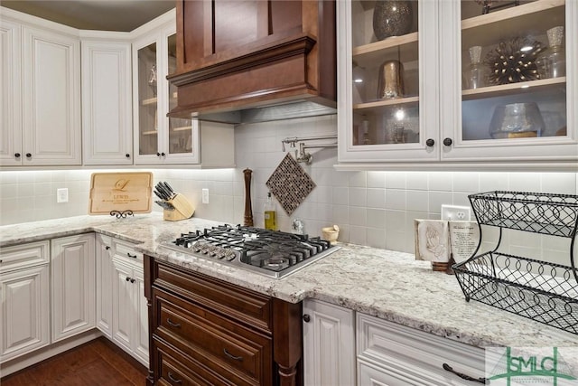 kitchen with custom exhaust hood, stainless steel gas stovetop, glass insert cabinets, and white cabinets