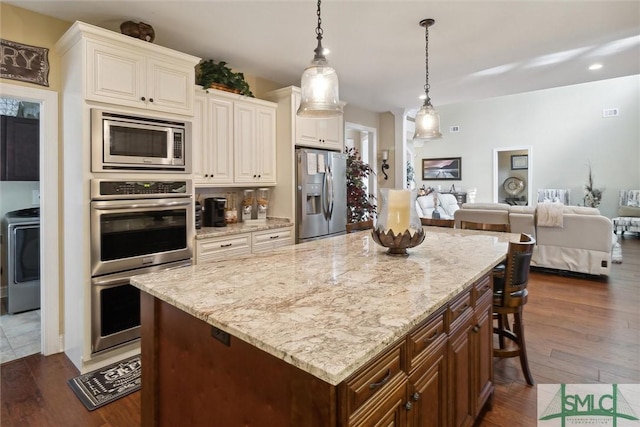 kitchen featuring stainless steel appliances, open floor plan, washer / clothes dryer, a kitchen bar, and pendant lighting