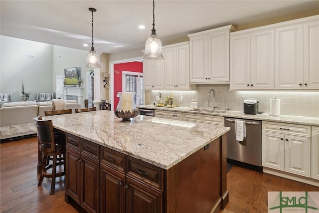 kitchen with pendant lighting, a breakfast bar area, stainless steel dishwasher, open floor plan, and a sink