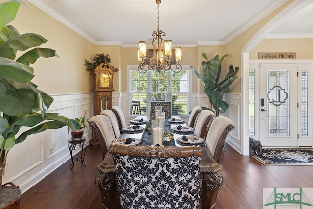 dining space with dark wood-style floors, a decorative wall, crown molding, and a notable chandelier