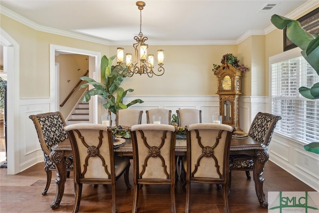 dining area featuring crown molding, a notable chandelier, visible vents, a decorative wall, and wood finished floors