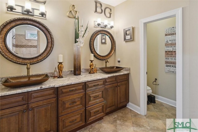 bathroom with baseboards, a sink, toilet, and double vanity