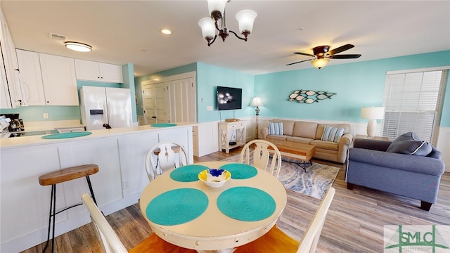 dining room with ceiling fan with notable chandelier and light hardwood / wood-style flooring