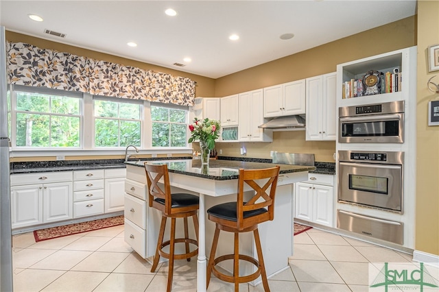 kitchen featuring a center island, a warming drawer, light tile patterned floors, visible vents, and under cabinet range hood