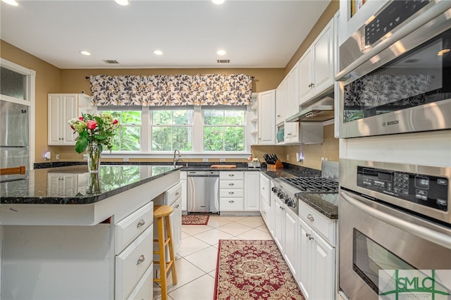 kitchen with white cabinets, stainless steel appliances, dark stone counters, and light tile patterned flooring