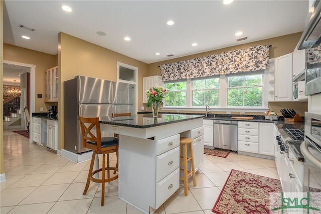 kitchen with dark stone countertops, light tile patterned floors, stainless steel appliances, a center island, and a breakfast bar area