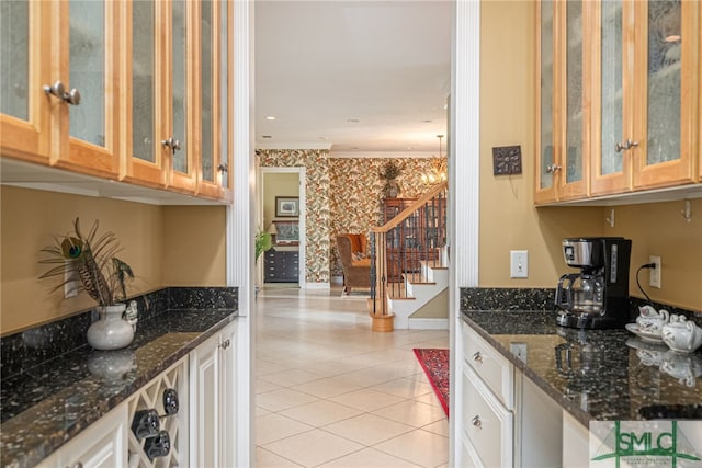 kitchen with glass insert cabinets, light tile patterned flooring, dark stone countertops, baseboards, and wallpapered walls