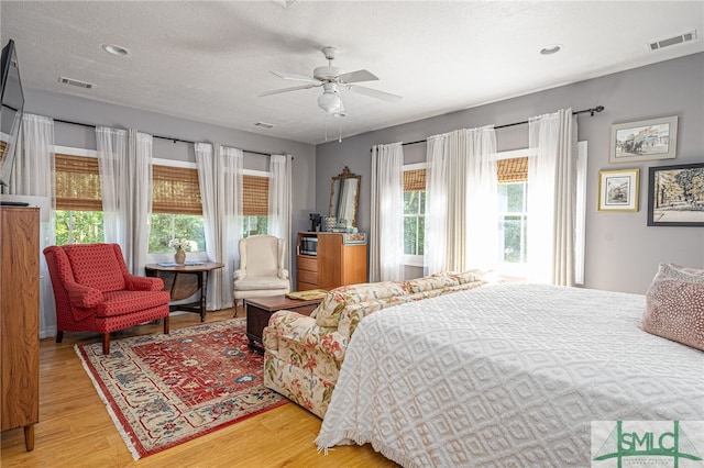 bedroom featuring light wood-type flooring, visible vents, ceiling fan, and a textured ceiling