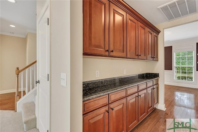 interior space with hardwood / wood-style floors, dark stone countertops, and crown molding