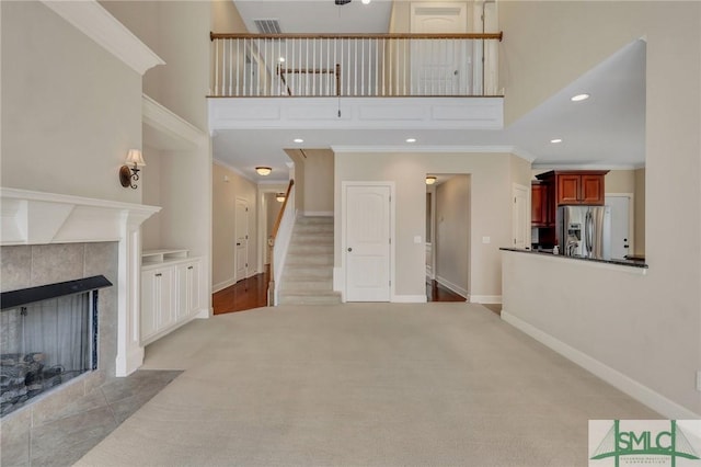 living room featuring light carpet, a high ceiling, a tile fireplace, and crown molding