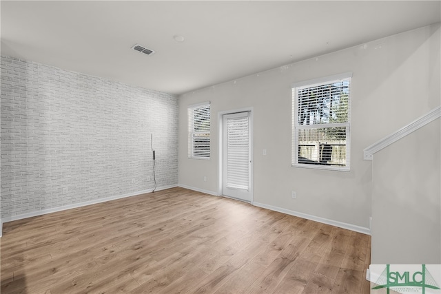 unfurnished room with light wood-type flooring, visible vents, baseboards, and brick wall