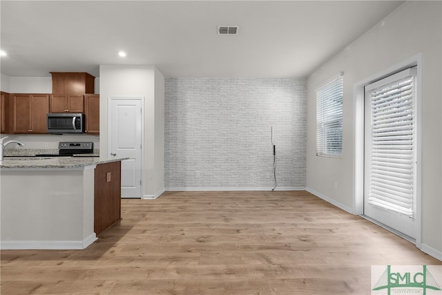 kitchen featuring brown cabinetry, visible vents, brick wall, light wood-style flooring, and stainless steel appliances