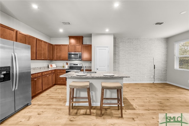 kitchen featuring visible vents, brick wall, light wood finished floors, a sink, and stainless steel appliances