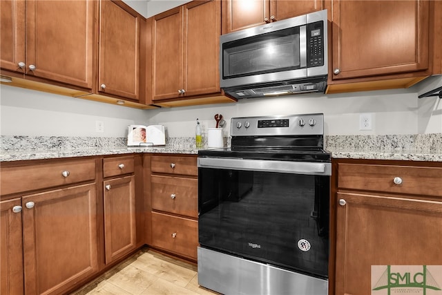 kitchen featuring light stone counters, stainless steel appliances, and brown cabinetry