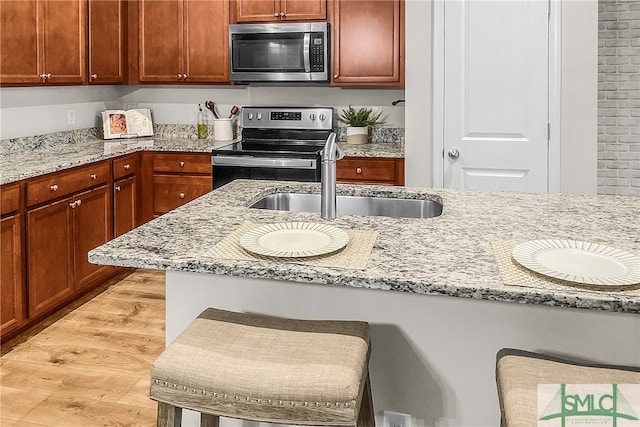 kitchen with a sink, light wood-type flooring, light stone countertops, and appliances with stainless steel finishes