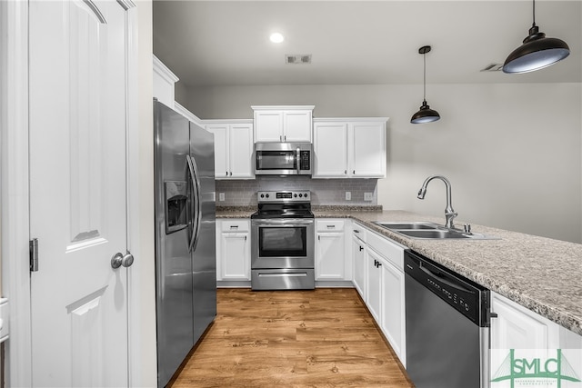 kitchen with light wood-type flooring, stainless steel appliances, sink, pendant lighting, and white cabinets