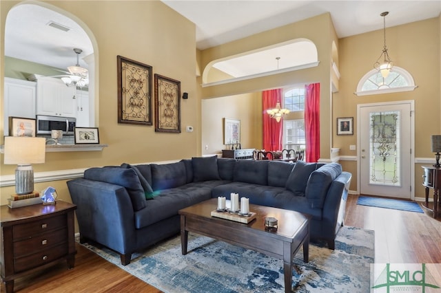 living room with ceiling fan, light wood-type flooring, and a towering ceiling